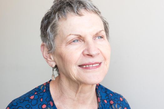 Closeup of older woman in blue top looking up hopefully against neutral background