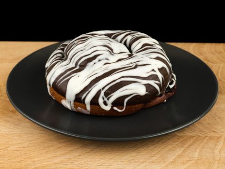 bun covered with chocolate, on a wooden board, on a black background