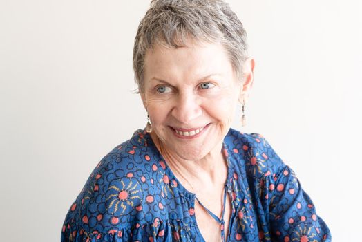 Older woman with drop earrings and blue top laughing against neutral background