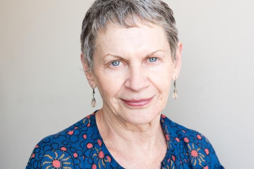 Portrait of older woman with drop earrings and blue top against neutral background