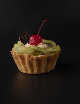 Fruit dessert cake with cherries, shecolade leaf, kiwi wedges and protein cream, on a black background isolated
