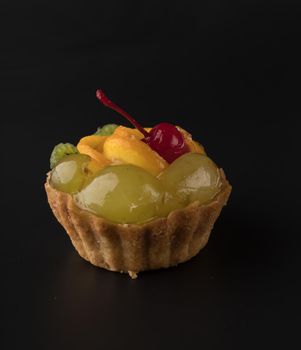 Fruit dessert cake with cherry grapes, kiwi and citrus fruits, on black background isolated