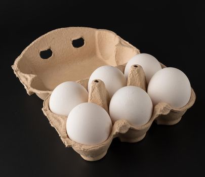 Chicken eggs, in the amount of six pieces in a disposable paper tray, on a black background, isolated