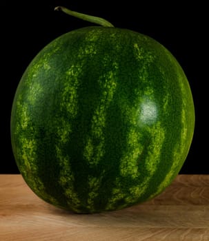 Whole watermelon, on wood board, on black background