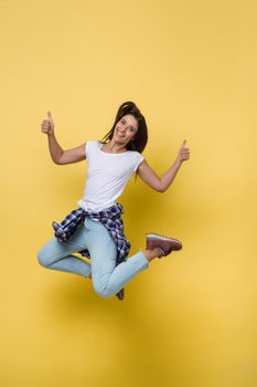 Full length portrait of a cheerful casual caucasian woman jumping isolated over yellow background.