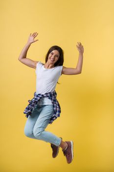 Full-length portrait of carefree girl in white shirt and jean jumping on yellow background