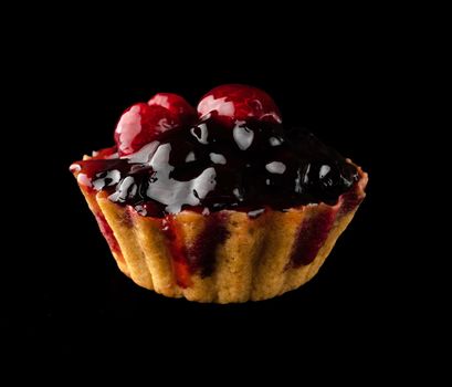 Pastry stuffed with berries and citrus fruits on a black background isolated, side view, confectionery product.