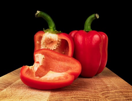 ripe red bell pepper, whole and in parts, on a board on a black background