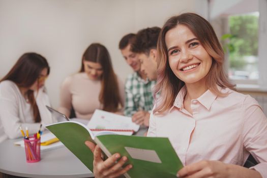 Knowledge, intelligence concept. Happy beautiful female college student smiling to the camera, while preparing for exams with her friends