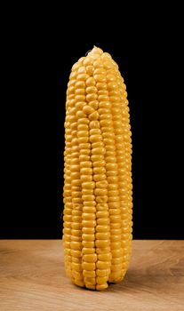 Ripe corn in a head of cabbage half peeled, on a wooden board and a black background