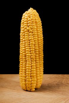 One swing of young peeled corn on a wooden board on a black background, close-up