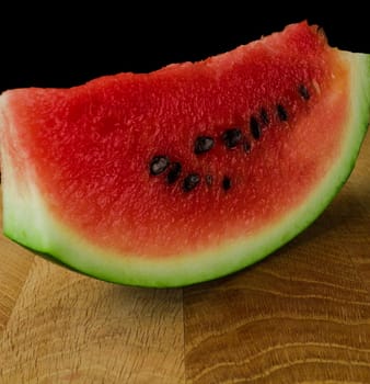 Sliced skib of ripe watermelon, on a wooden board, on a black background