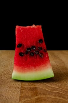 Piece of ripe watermelon, on a wooden board, on a black background