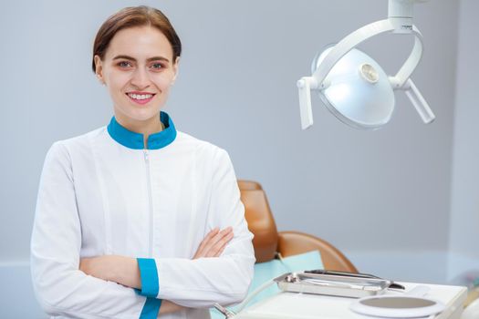 Portrait of a happy beautiful female dentist posing proudly at her dental clinic, copy space. Cheerful dentist in uniform smiling confidently to the camera with her arms crossed. Medicine, health