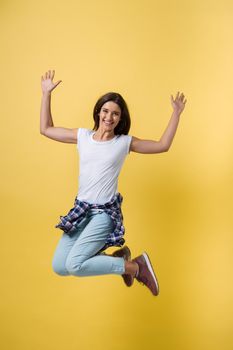 Full length portrait of a cheerful casual caucasian woman jumping isolated over yellow background.