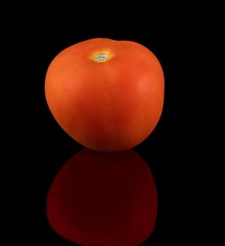 One ripe tomato on a black background, with reflection