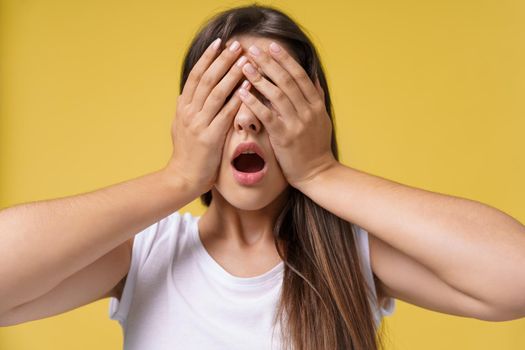 Happy surprised excited woman covering with hands her eye with blank copy space,Portrait beautiful woman. Positive human emotion expression,isolated on yellow background.