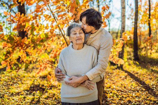 Grandmother and adult grandson hugging in autumn park.