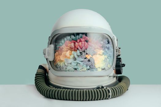 Closed astronaut helmet filled with colorful chrysanthemum flowers on mint color background. Cosmonaut space helmet with flowers. Abstract space beauty concept