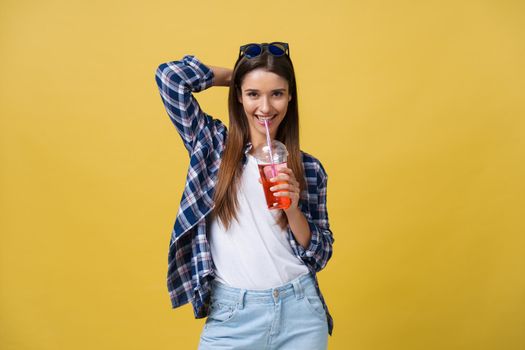 Fashion pretty young woman with fresh fruit juice cup in blue shirt having fun over colorful yellow background.