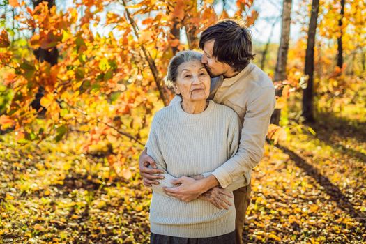 Grandmother and adult grandson hugging in autumn park.