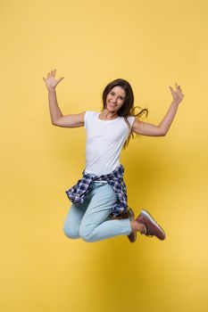 Full-length portrait of carefree girl in white shirt and jean jumping on yellow background