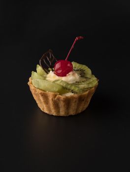 Fruit dessert cake with cherries, shecolade leaf, kiwi wedges and protein cream, on a black background isolated