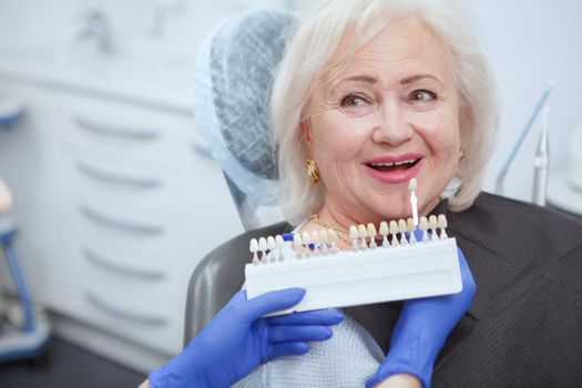 Unrecognizable dentist choosing teeth whitening shade for her senior patient, copy space