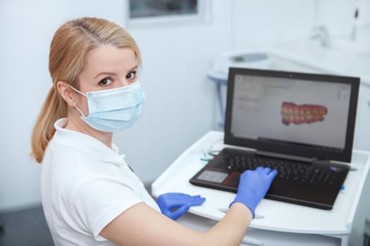 Female dentist wearing medical face mask, looking to the camera while working on her computer