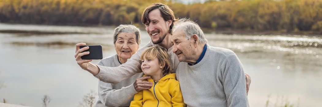 BANNER, LONG FORMAT Senior couple with grandson and great-grandson take a selfie in the autumn park. Great-grandmother, great-grandfather and great-grandson.