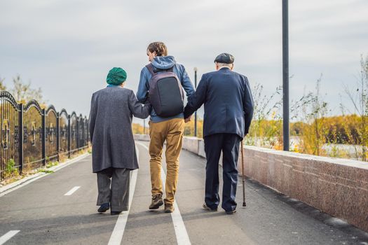 An elderly couple walks in the park with a male assistant or adult grandson. Caring for the elderly, volunteering.