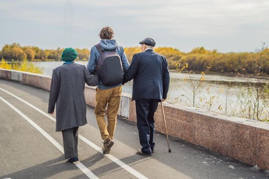 An elderly couple walks in the park with a male assistant or adult grandson. Caring for the elderly, volunteering.