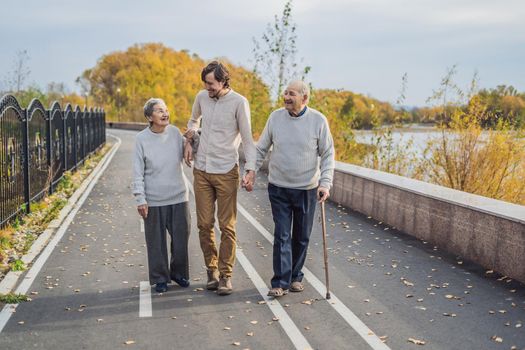 An elderly couple walks in the park with a male assistant or adult grandson. Caring for the elderly, volunteering.