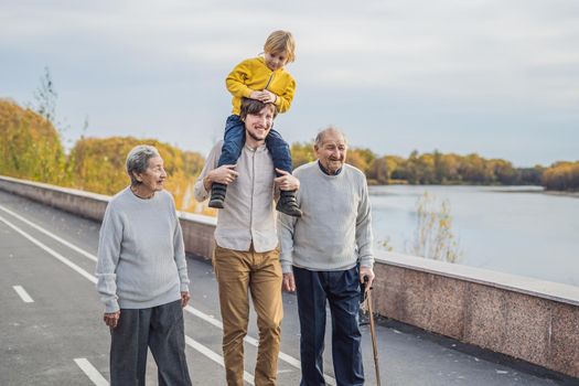 An elderly couple walks in the park with a river with their grandson and great-grandson.
