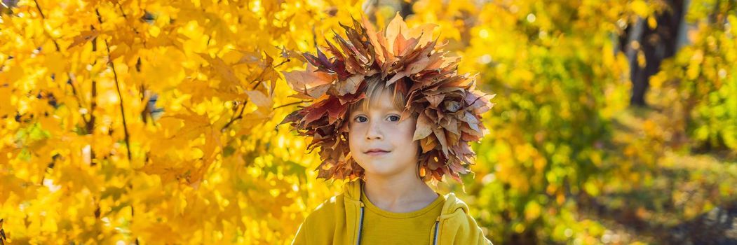 Portrait of little smiling child with wreath of leaves on head background of sunny autumn park. BANNER, LONG FORMAT
