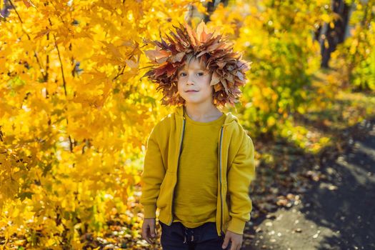 Portrait of little smiling child with wreath of leaves on head background of sunny autumn park.