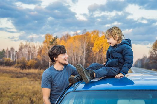 Dad and son are resting on the side of the road on a road trip. Road trip with children concept.