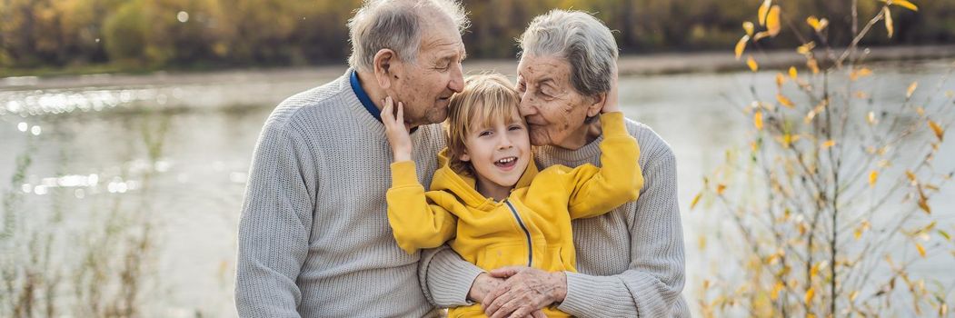 BANNER, LONG FORMAT Senior couple with baby grandson in the autumn park. Great-grandmother, great-grandfather and great-grandson.