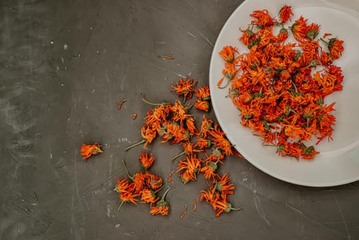 Dried flowers in a gray plate. Medicinal herbal dried plants marigold, orange calendula. Neutral white and gray background.