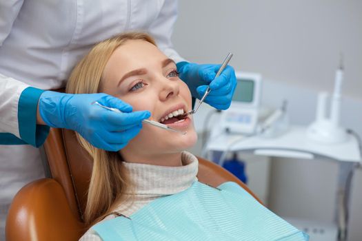 Cropped shot of a professional dentist examining teeth of a beautiful young woman. Attractive female smiling, while dentist checking her teeth. Dental appointment at the clinic. Medicine, health