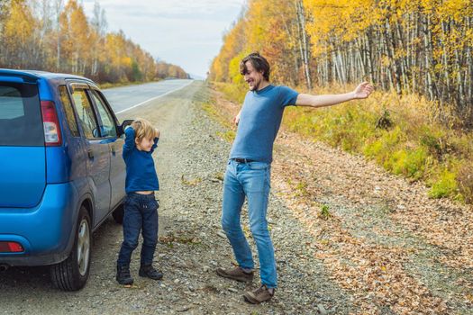 Dad and son are resting on the side of the road on a road trip. Road trip with children concept.