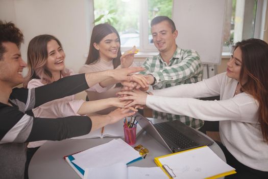 Togetherness, unity concept. Group of cheerful college students putting their hands together, showing unity. Happy young people stacking hands in a pile together