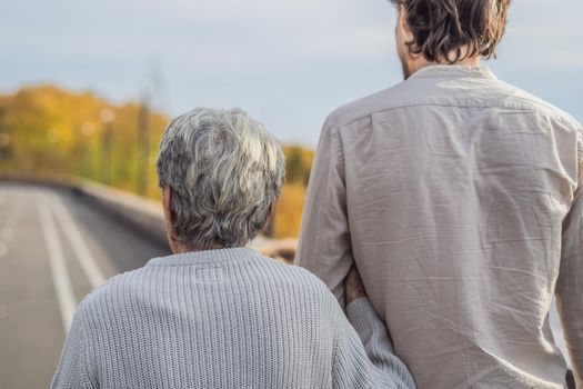 An elderly couple walks in the park with a male assistant or adult grandson. Caring for the elderly, volunteering.