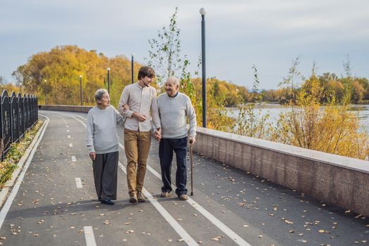 An elderly couple walks in the park with a male assistant or adult grandson. Caring for the elderly, volunteering.