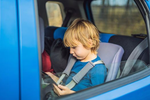 Little boy traveling on backseat of a car using touch pad to entertain himself during the trip.
