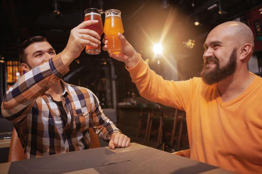 Low angle shot of two male friends celebrating at the beer pub, clinking their glasses