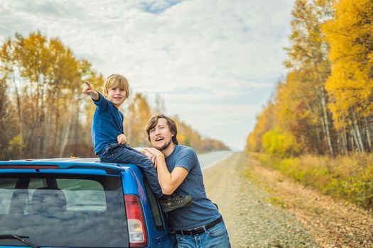 Dad and son are resting on the side of the road on a road trip. Road trip with children concept.