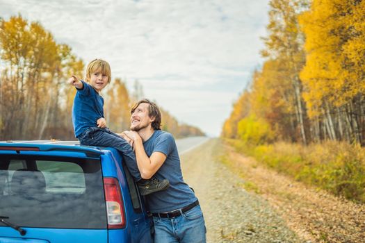 Dad and son are resting on the side of the road on a road trip. Road trip with children concept.