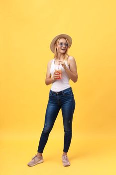 Full length portrait of a cheerful young woman wearing summer clothes while posing and looking at camera isolated over yellow summer background.