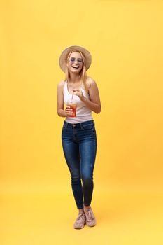 Full length portrait of a cheerful young woman wearing summer clothes while posing and looking at camera isolated over yellow summer background.